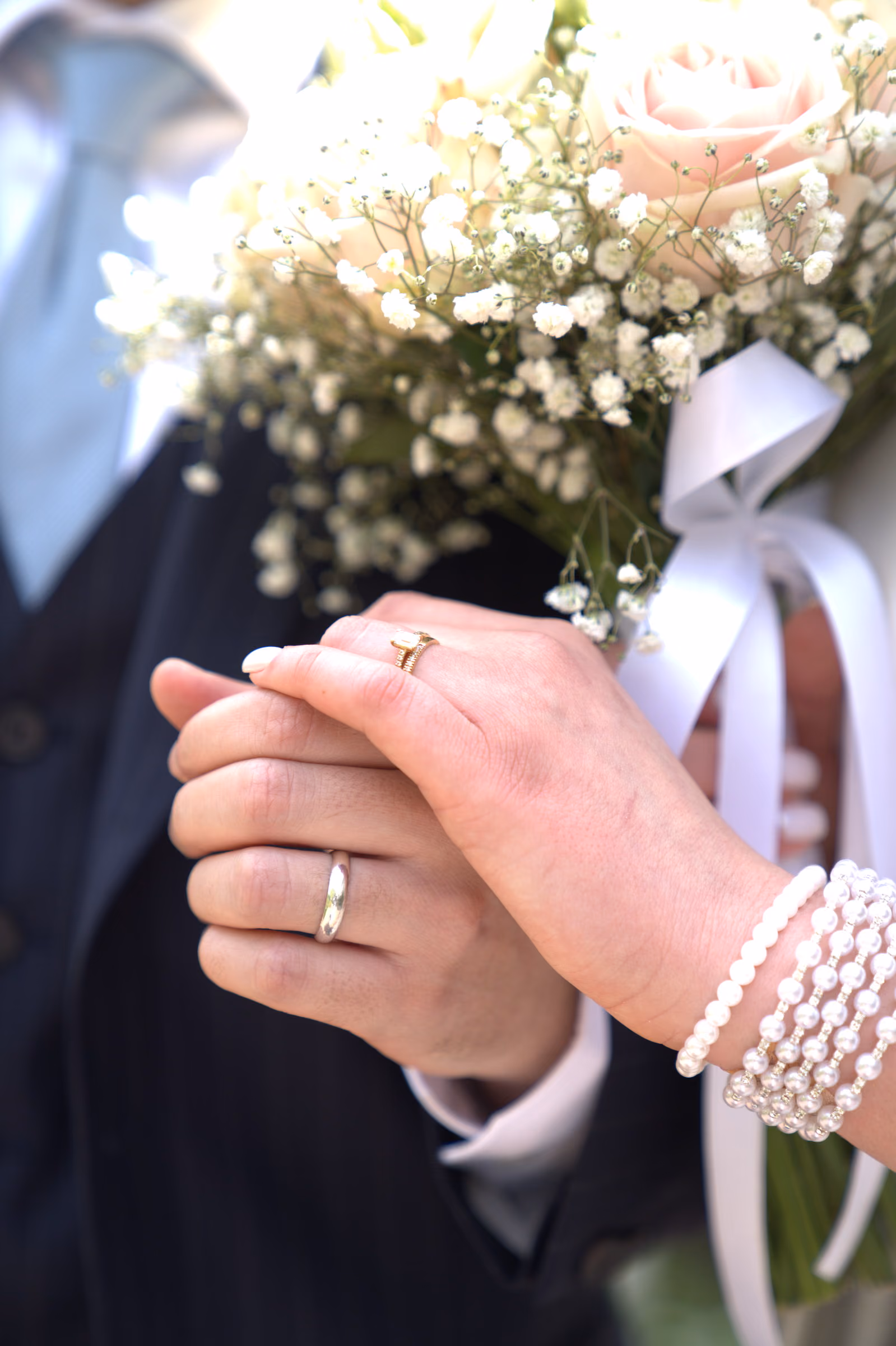 The couple’s hands joined in front of the bouquet, rings and a pearl bracelet