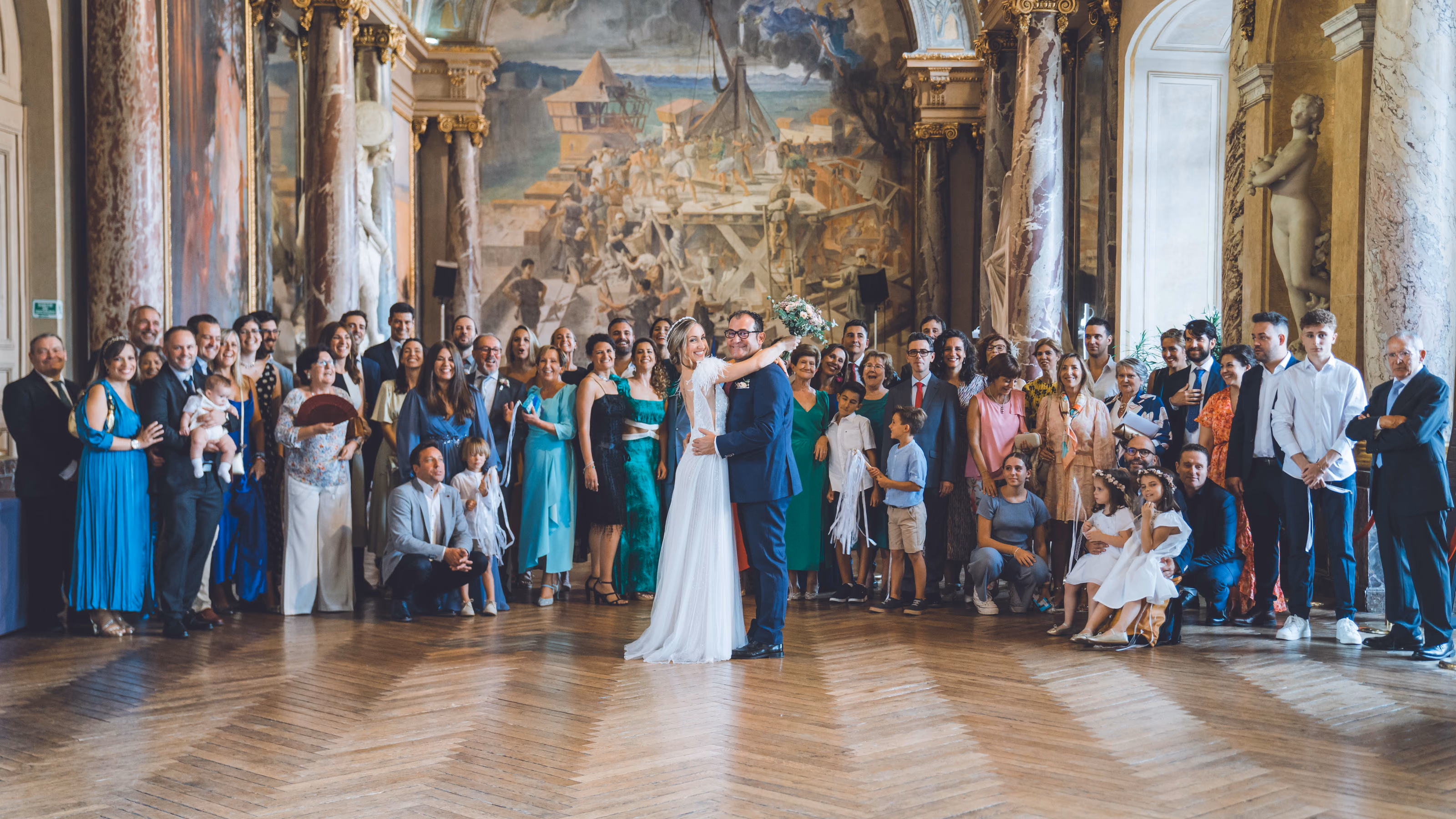 The couple embracing in front of all their guests, in a grand frescoed town hall room