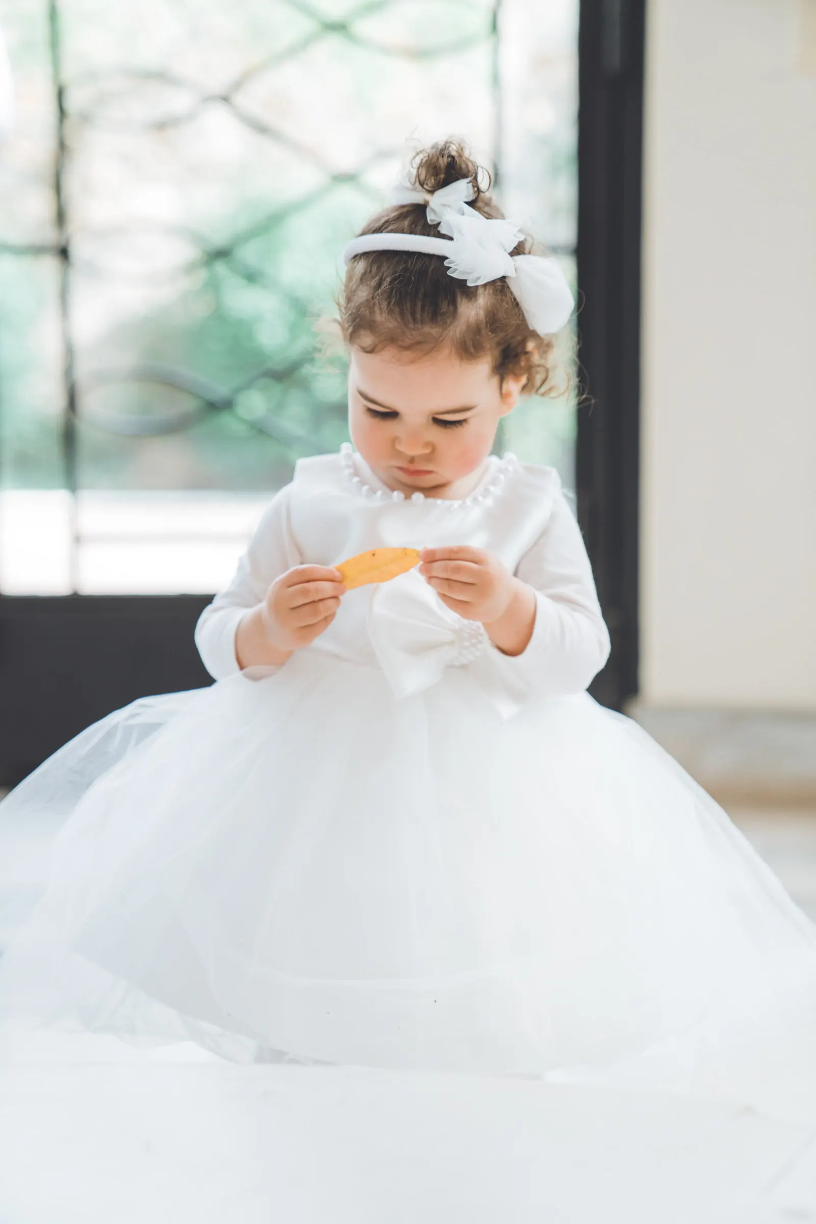 Une petite fille en robe de tulle blanche, une feuille entre les mains
