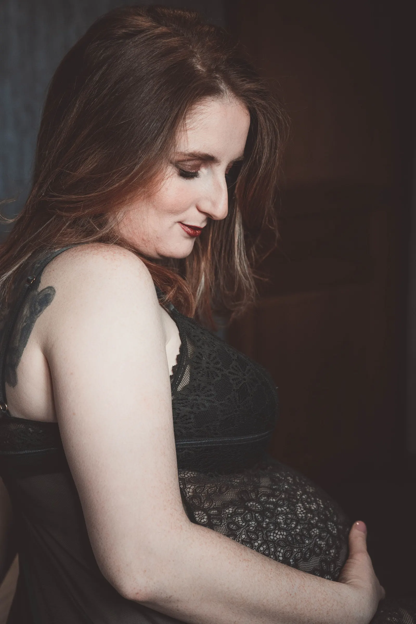 Une femme enceinte de profil, une main posée sur son ventre, dans une lumière douce et sombre