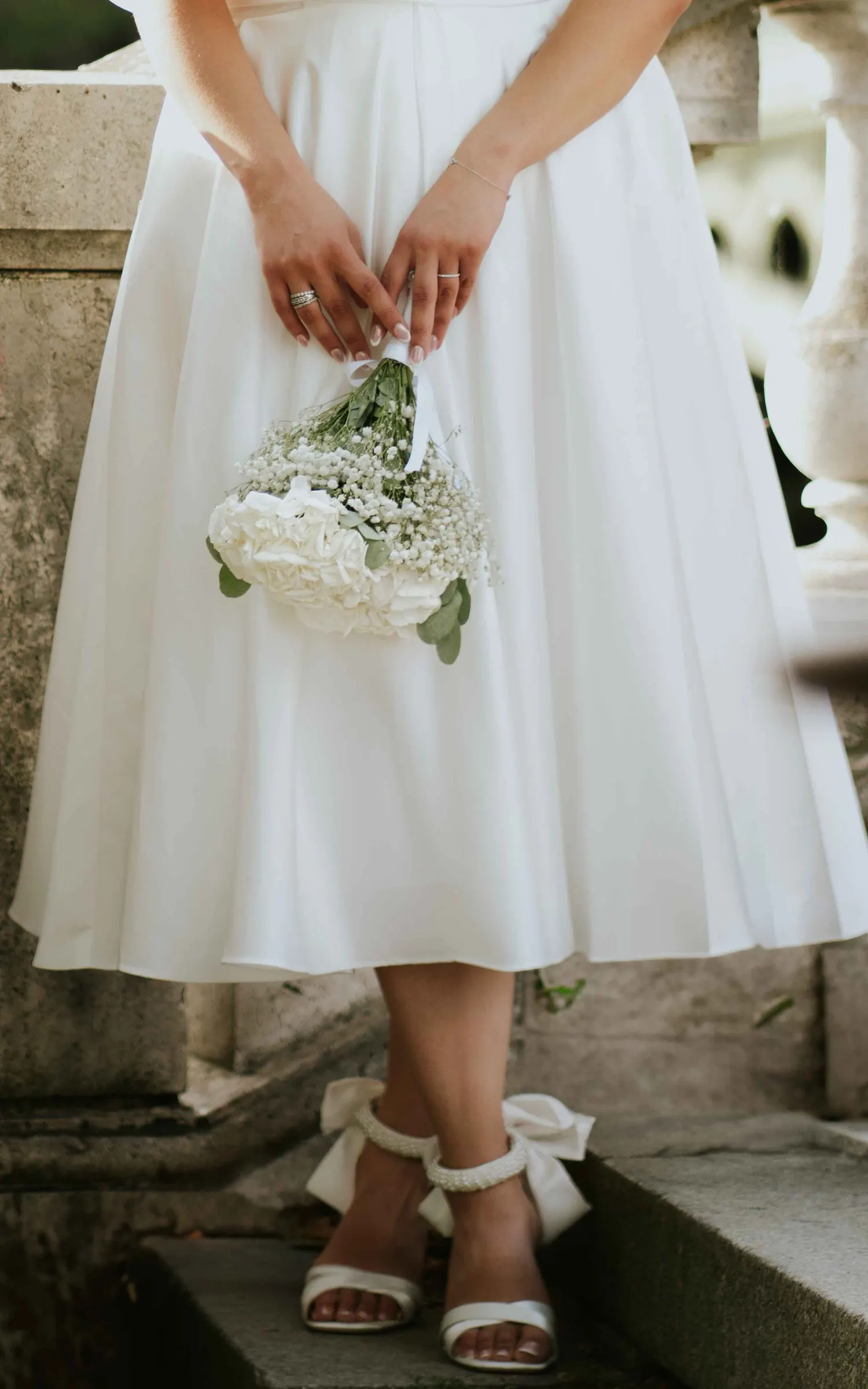Les mains de la mariée autour d’un bouquet blanc, robe courte
