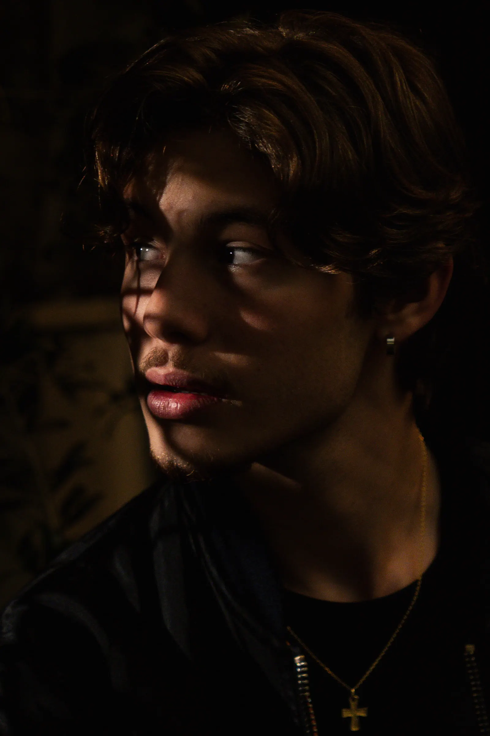 Portrait serré d’un jeune homme, une lumière rasante sur le visage, fond sombre