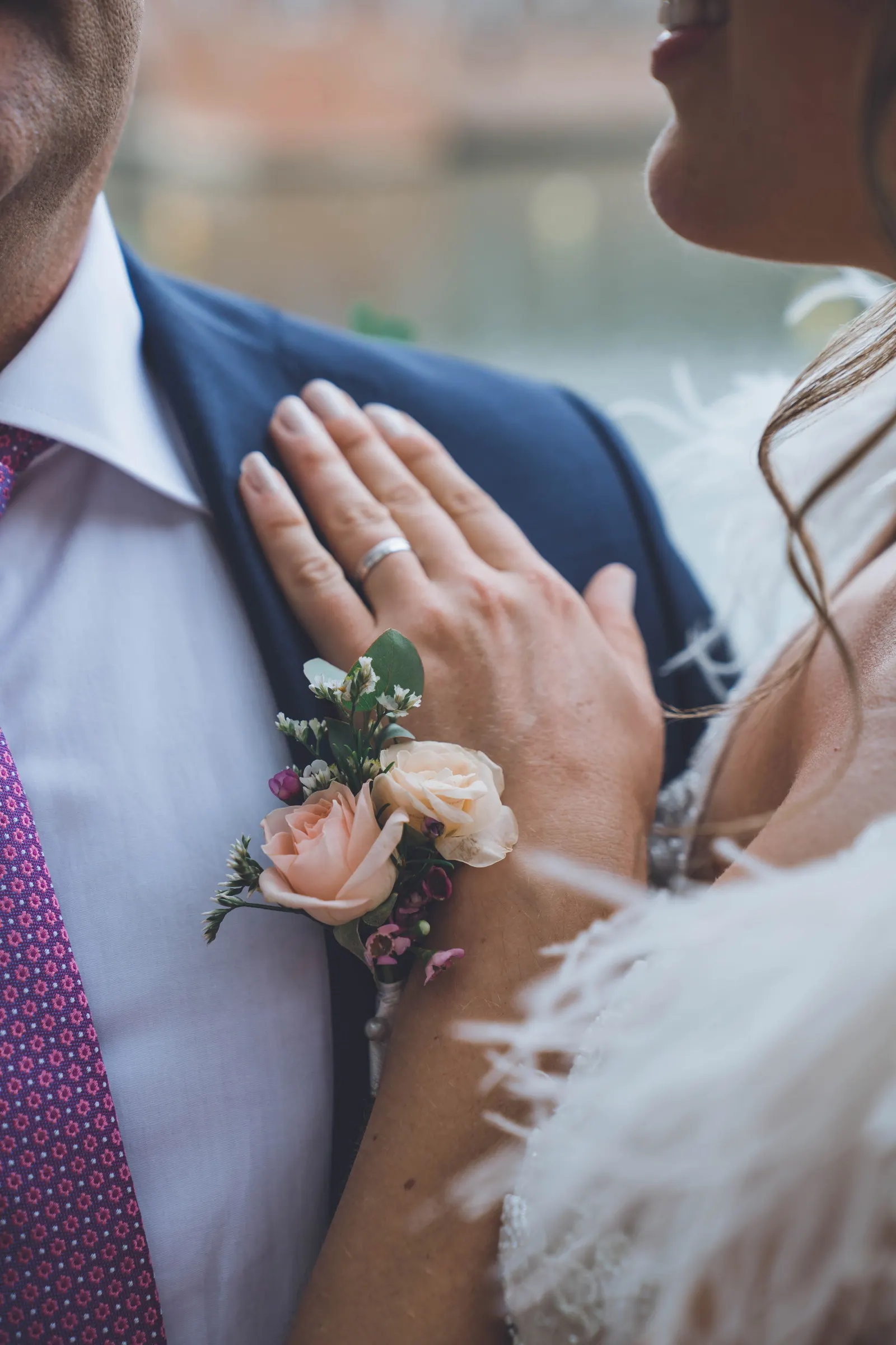Les mains des mariés l’un contre l’autre, la boutonnière au premier plan