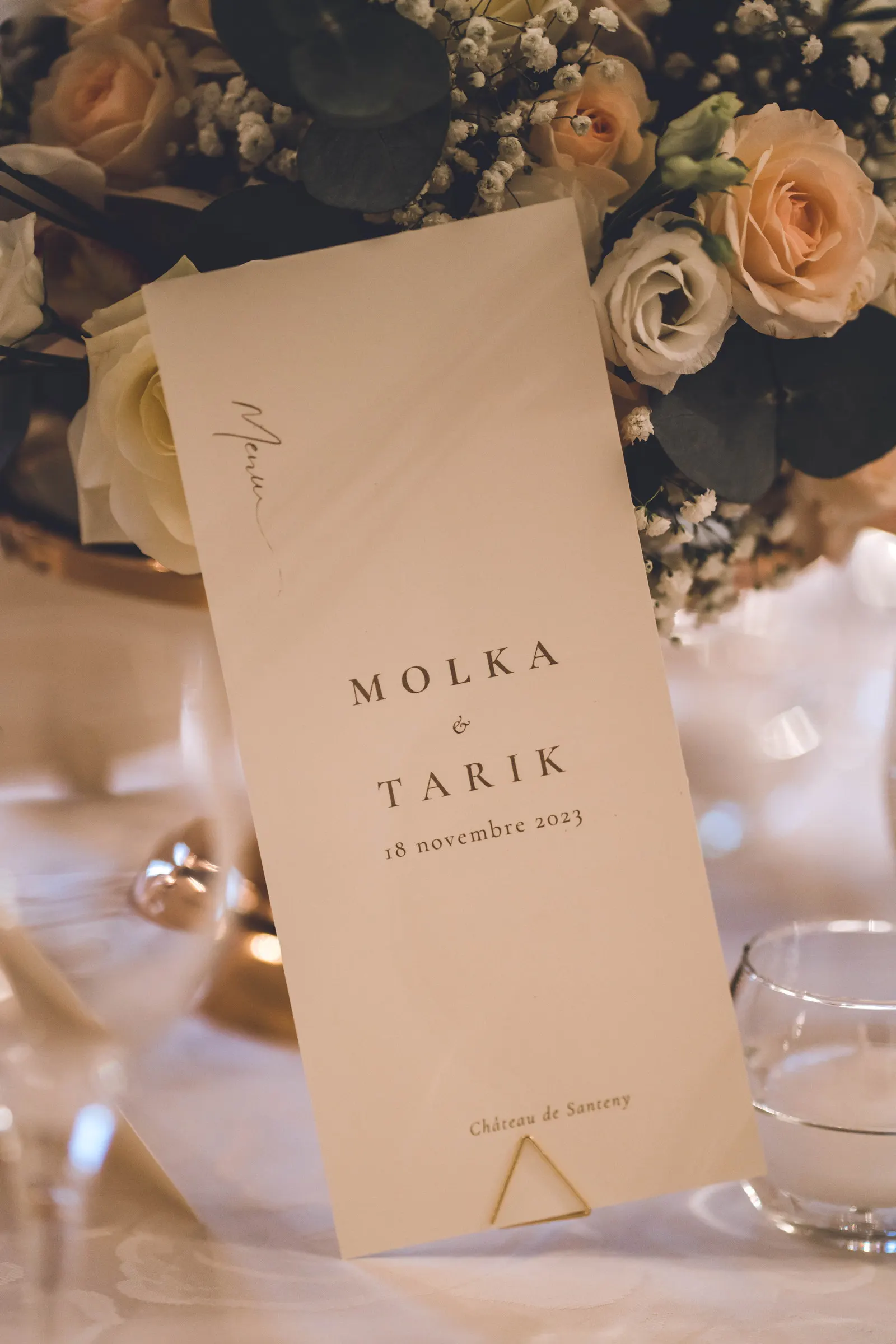 Un menu de mariage calligraphié posé près des alliances et de quelques fleurs