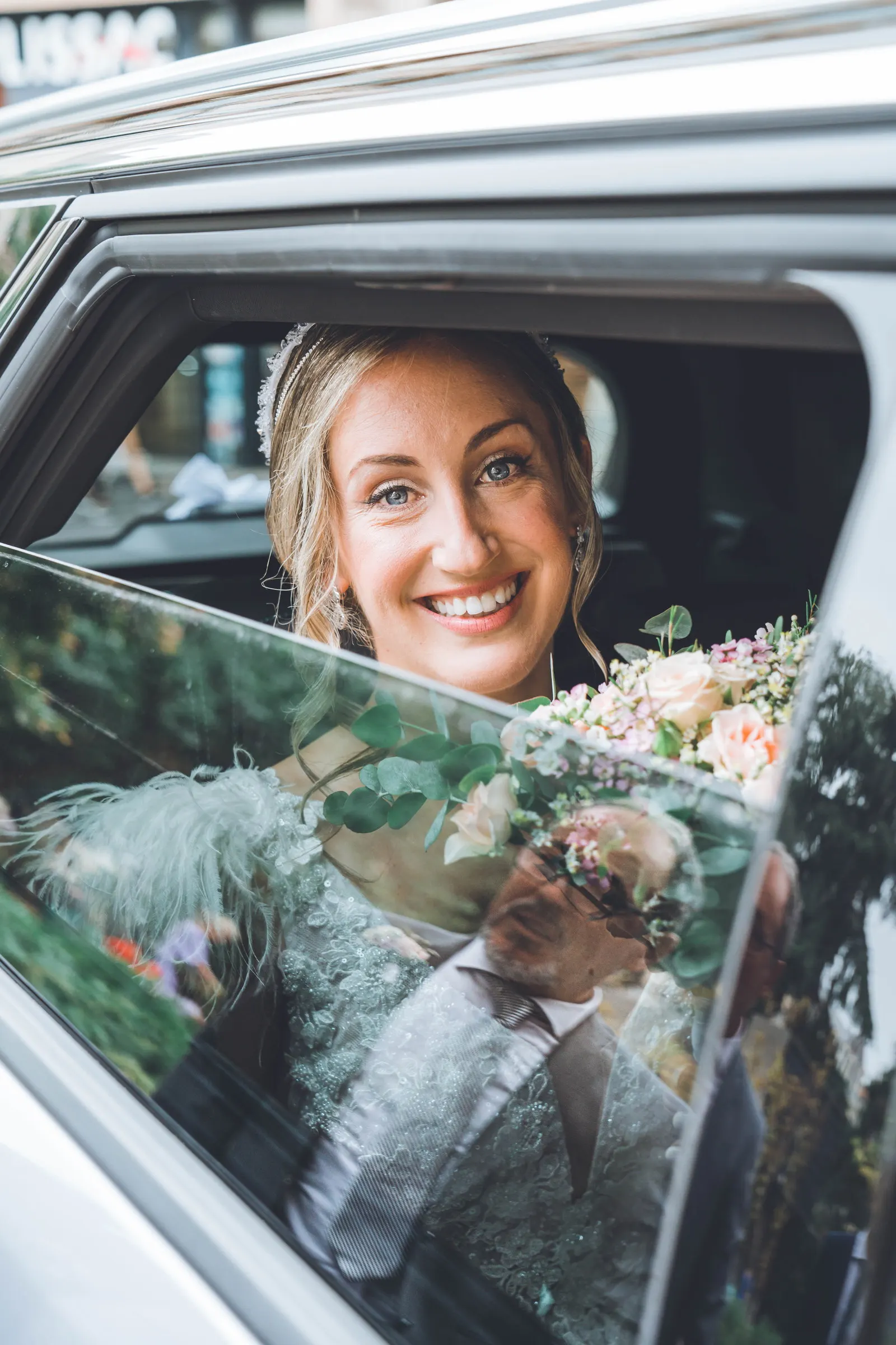 La mariée souriante à la vitre d’une voiture, le marié reflété dans le verre