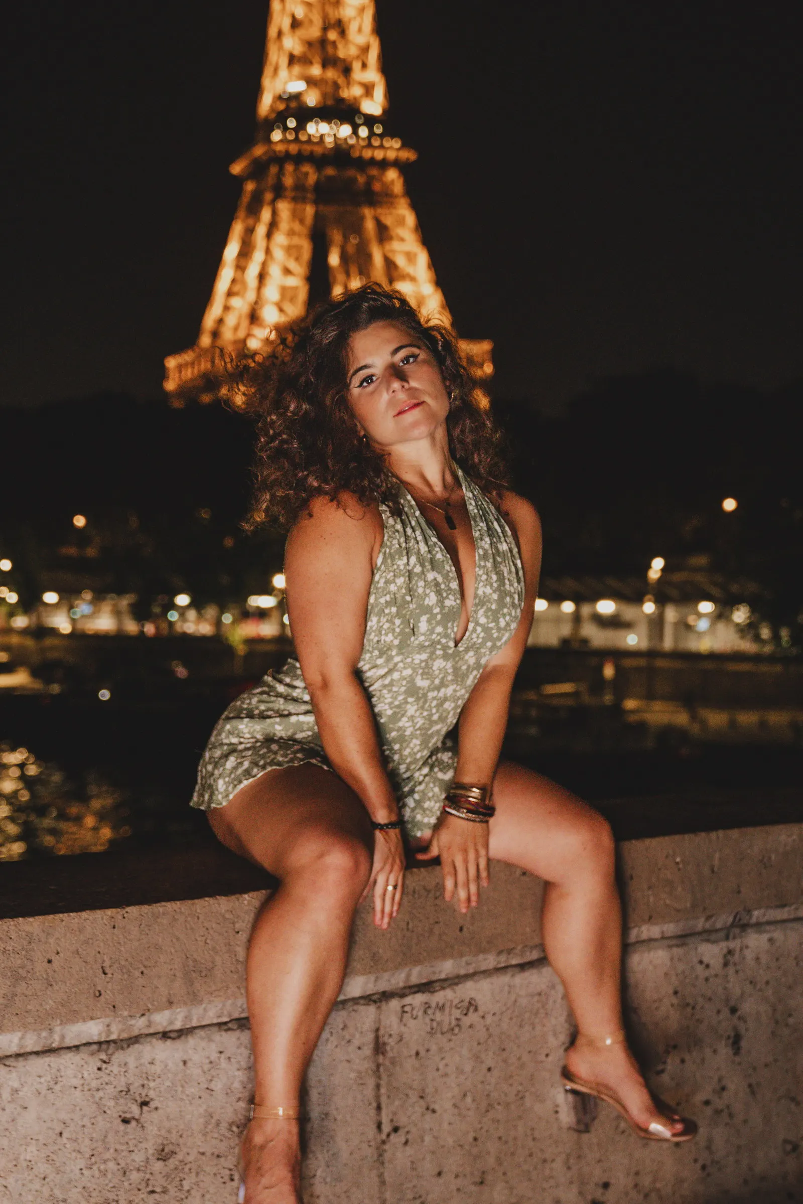 Une femme assise sur un parapet, la tour Eiffel illuminée derrière elle