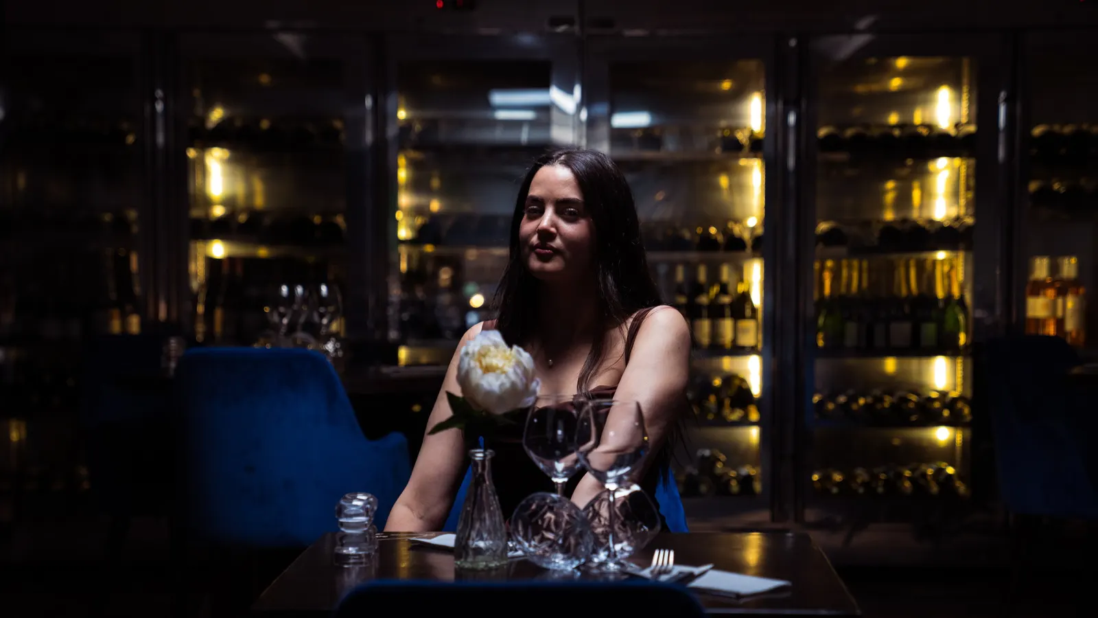 Une femme assise à un bar dans la pénombre, un verre à la main