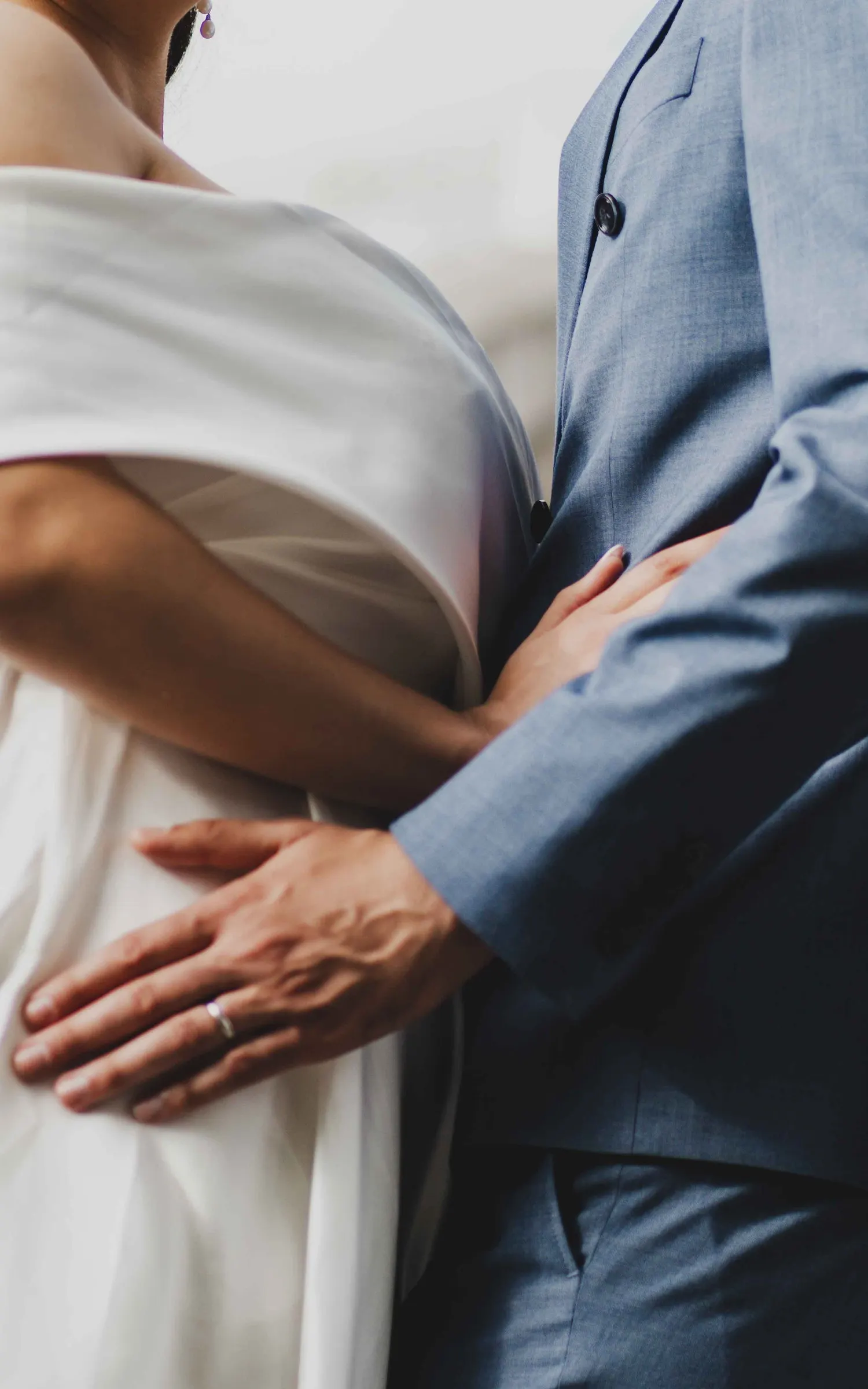 Une main posée à la taille de la mariée, manche de costume clair