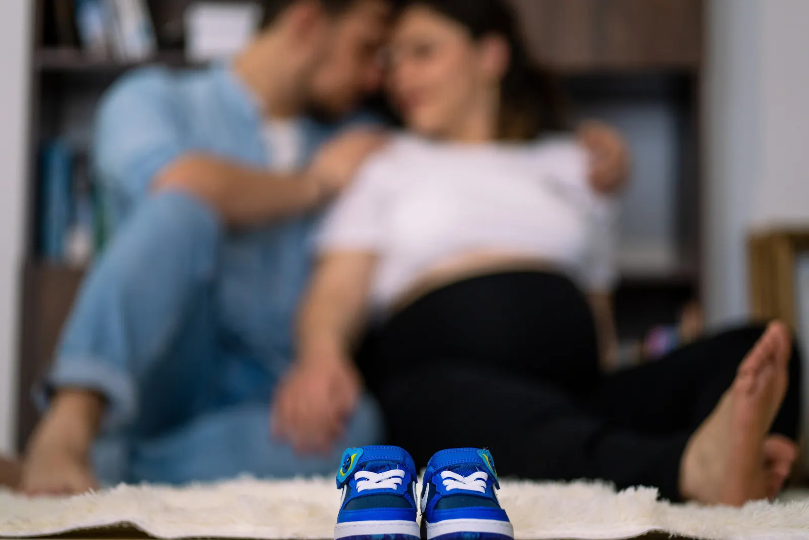Un couple assis au sol, une paire de chaussons de bébé posée devant eux