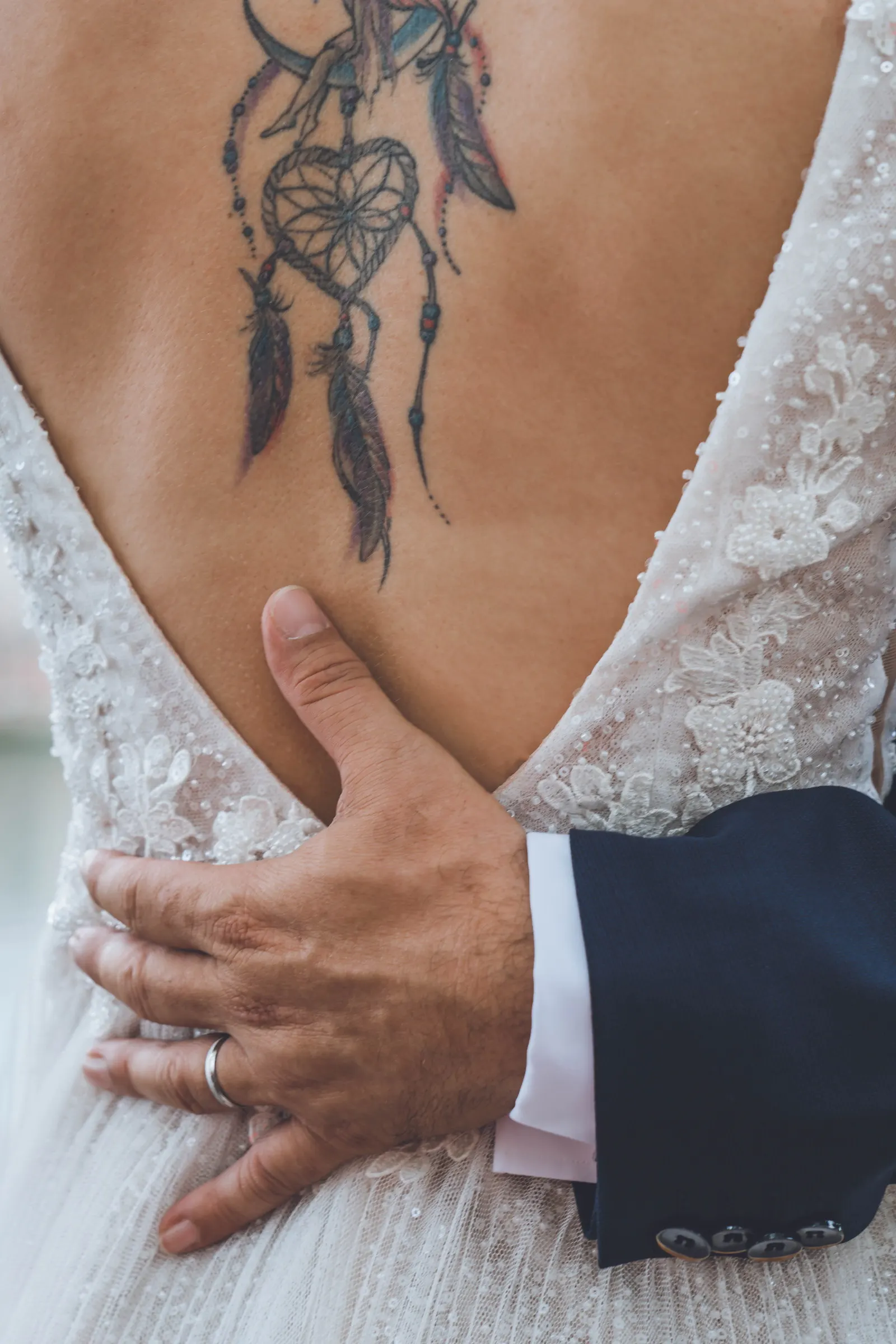 Une main posée dans le dos de la mariée, sur une robe en dentelle au dos ouvert